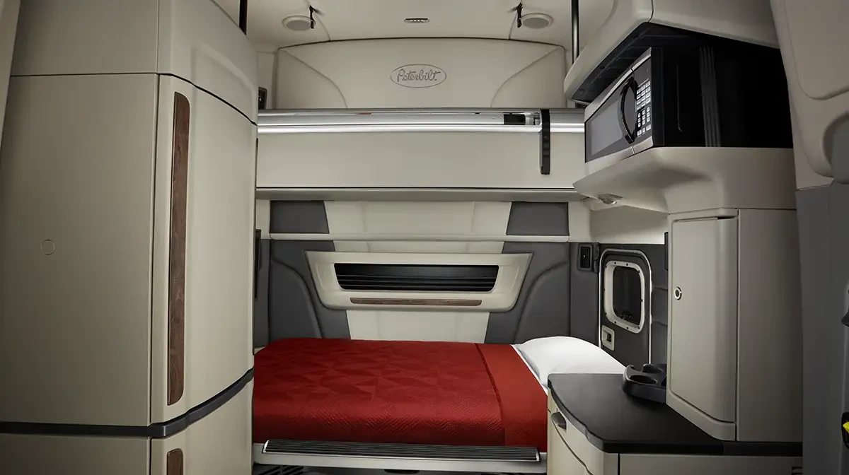 Inside view of a Peterbilt 579 ultraloft sleeper cab with beige and grey interior with red bedding.